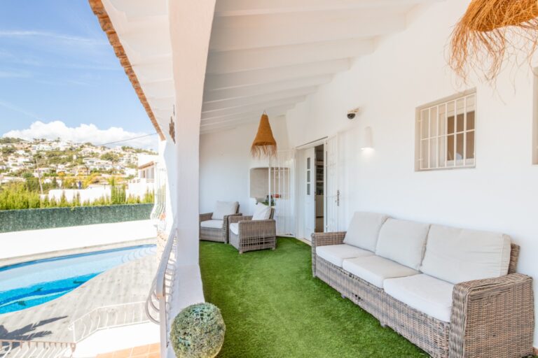 Covered terrace at a renovated Mediterranean villa in Moraira with outdoor sofa seating, private pool views, white arches and shaded lounge space