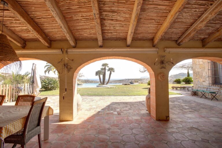 Covered terrace at a rustic Mediterranean estate near Moraira with arched openings, timber ceiling, outdoor dining area and garden views