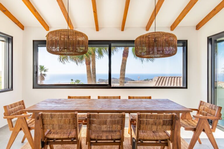 Dining area inside a luxury smart home villa near Moraira with wooden beams, large window, sea views, natural light and wooden dining furniture