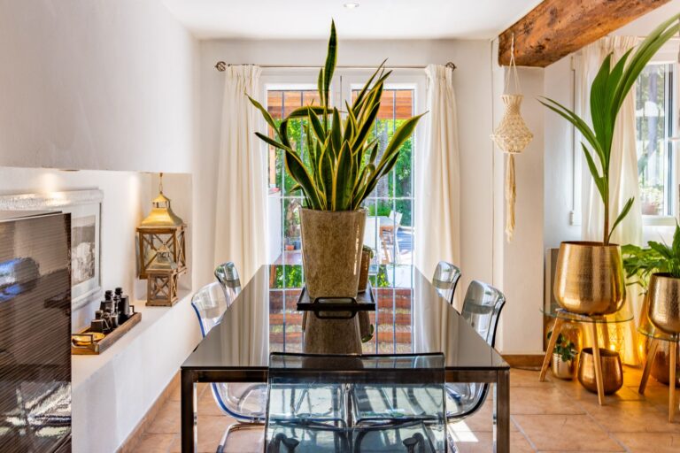 Dining area inside a Mediterranean villa near Cala Baladrar in Benissa Costa with fireplace, glass dining table, indoor plants and natural light