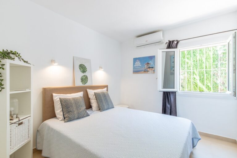 Double bedroom inside a renovated Mediterranean villa in Moraira with air conditioning, bright window, white furnishings and neutral interior