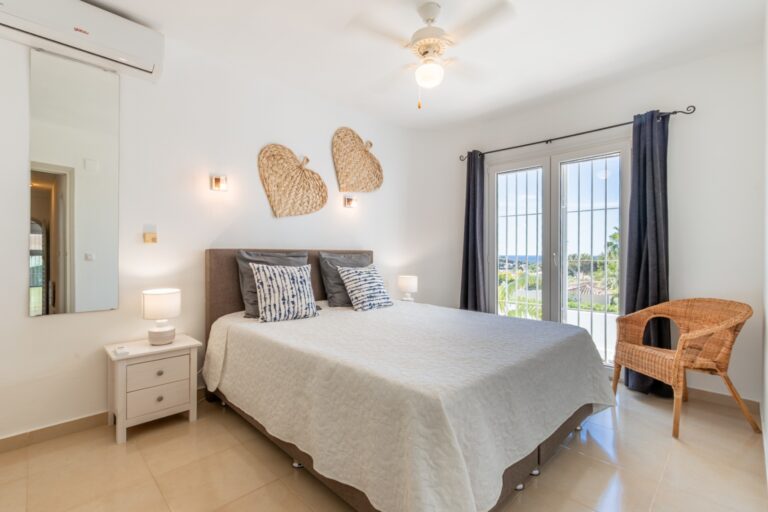 Double bedroom inside a renovated Mediterranean villa in Moraira with fitted storage, ceiling fan, bright windows and neutral interior