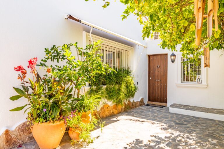 Entrance at a Mediterranean villa near Cala Baladrar in Benissa Costa with garden path, mature planting, wooden door and white exterior walls