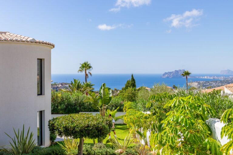 Garden and sea views from a luxury villa near Moraira with Mediterranean planting, palm trees, surrounding homes and Peñón de Ifach in the distance