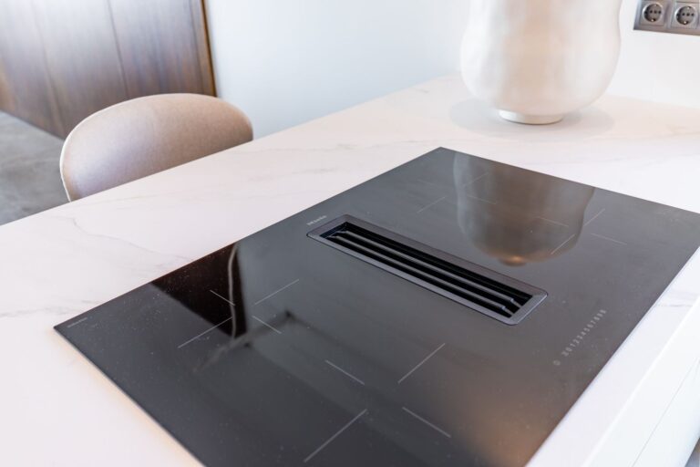Induction hob detail inside a luxury smart home villa near Moraira with white worktop, integrated extractor and premium kitchen finish