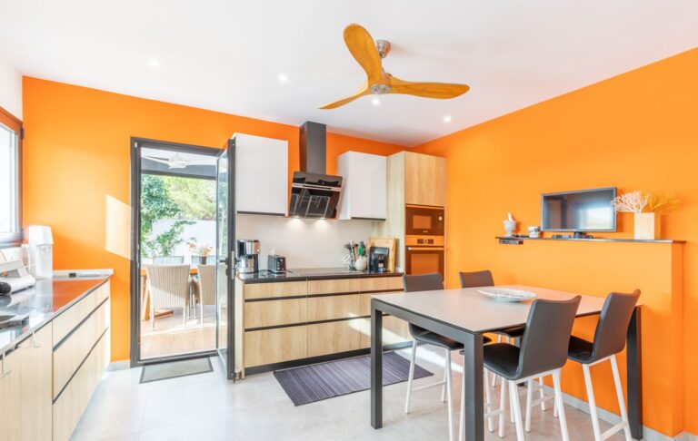 Kitchen and dining area inside a modern villa in Pla del Mar, Moraira with orange feature wall, fitted appliances, island and contemporary finish