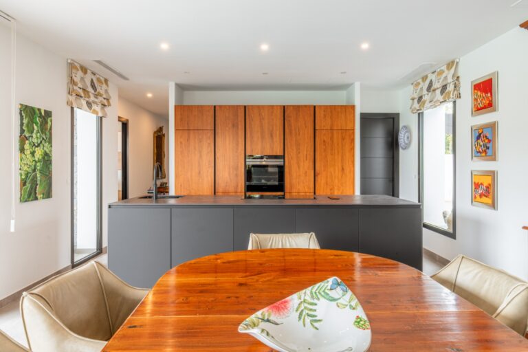 Kitchen and dining area inside a modern villa in Solpark, Moraira with DEKTON island, wooden cabinetry, dining table and bright contemporary interior