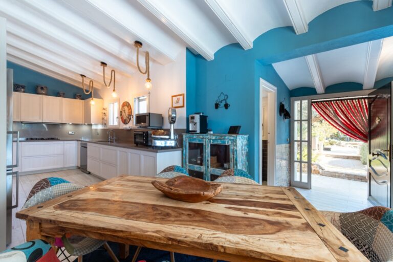 Kitchen and dining area inside a renovated finca near Teulada and Moraira with blue feature wall, wooden dining table, white beamed ceiling and terrace access