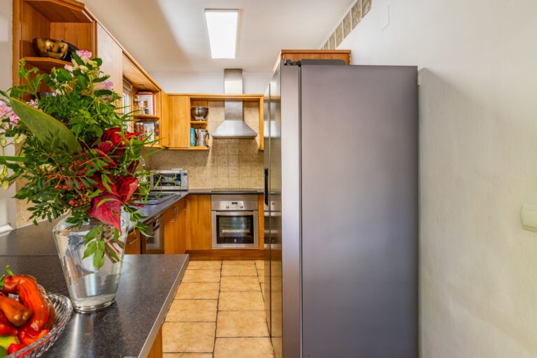 Kitchen and dining detail inside a Mediterranean villa near Cala Baladrar in Benissa Costa with wooden cabinetry, tiled flooring, plants and worktop space