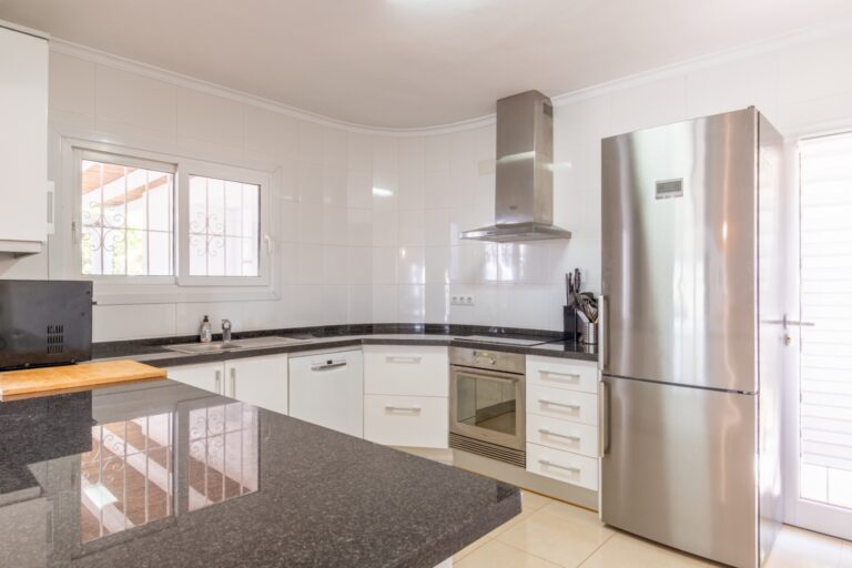 Kitchen inside a renovated Mediterranean villa in Moraira with white cabinetry, large worktop, modern appliances and bright windows