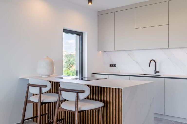 Kitchen island inside a luxury smart home villa near Moraira with breakfast bar seating, white cabinetry, large window and premium contemporary finish