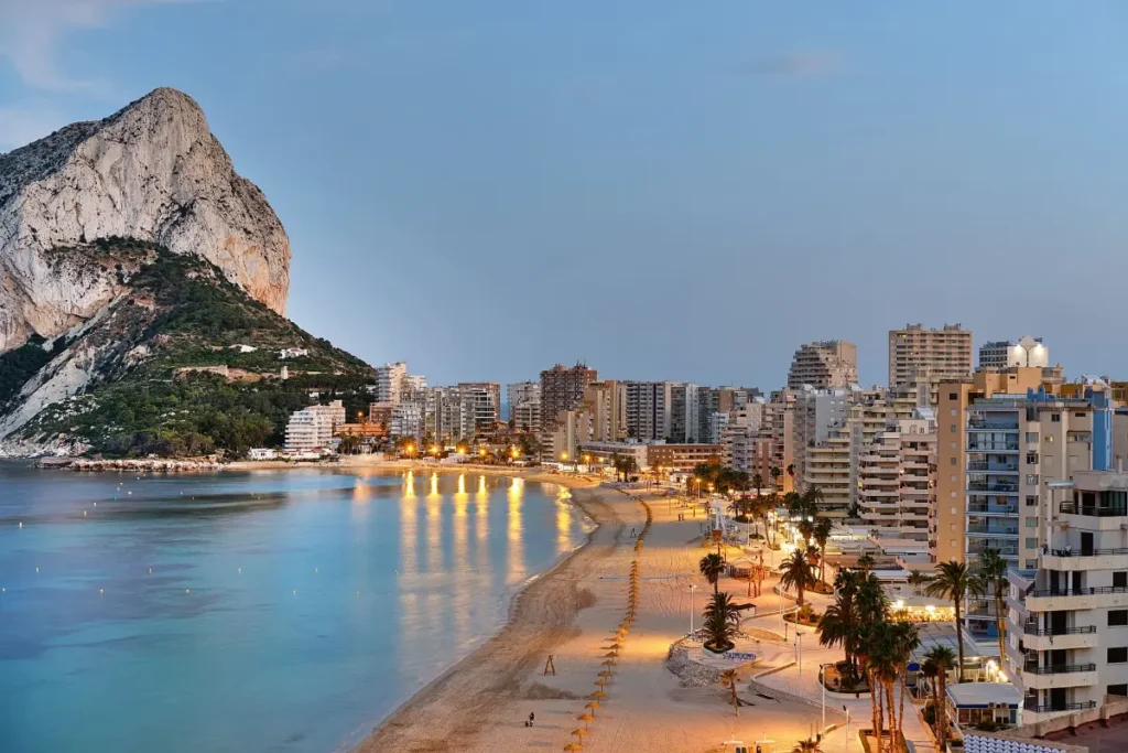 La Fossa Beach in Calpe at evening with Peñón de Ifach and beachfront apartments illuminated along the promenade