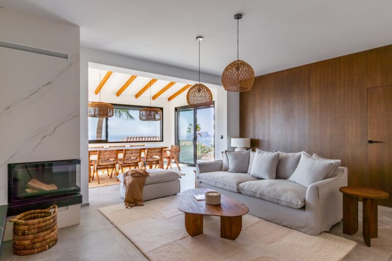 Living room inside a luxury smart home villa near Moraira with fireplace, sofa seating, open-plan dining area, wooden wall finish and natural light
