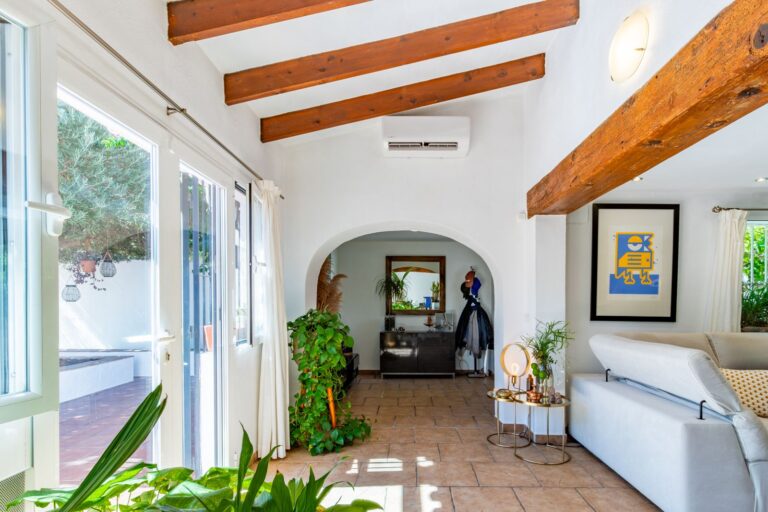 Living room inside a Mediterranean villa near Cala Baladrar in Benissa Costa with exposed wooden beams, arched doorway, terrace access and natural light