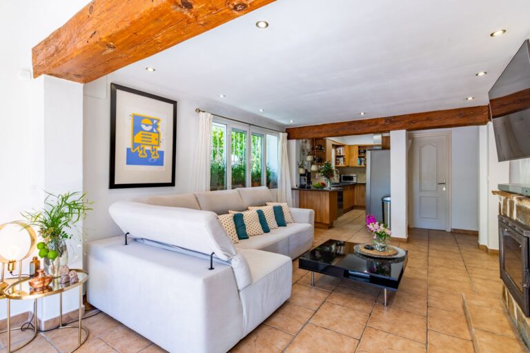 Living room inside a Mediterranean villa near Cala Baladrar in Benissa Costa with sofa seating, kitchen view, exposed wooden beams and stone fireplace
