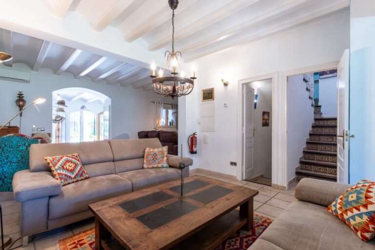 Living room inside a renovated finca near Teulada and Moraira with sofa seating, coffee table, white beamed ceiling and staircase view
