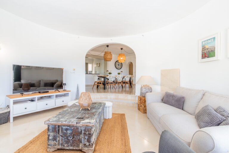 Living room inside a renovated Mediterranean villa in Moraira with sofa seating, TV area, arched opening to the dining room and bright interior
