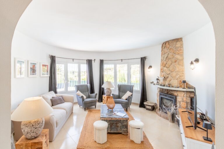 Living room inside a renovated Mediterranean villa in Moraira with stone fireplace, curved windows, sofa seating and bright interior