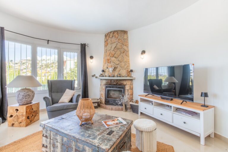 Living room inside a renovated Mediterranean villa in Moraira with stone fireplace, sofa seating, TV area and large windows