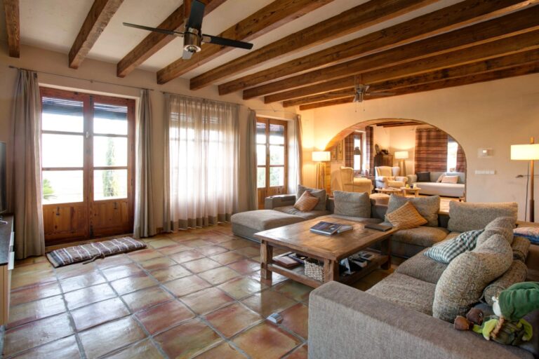 Lounge inside a rustic Mediterranean estate near Moraira with exposed timber beams, terracotta flooring, sofa seating and arched doorway