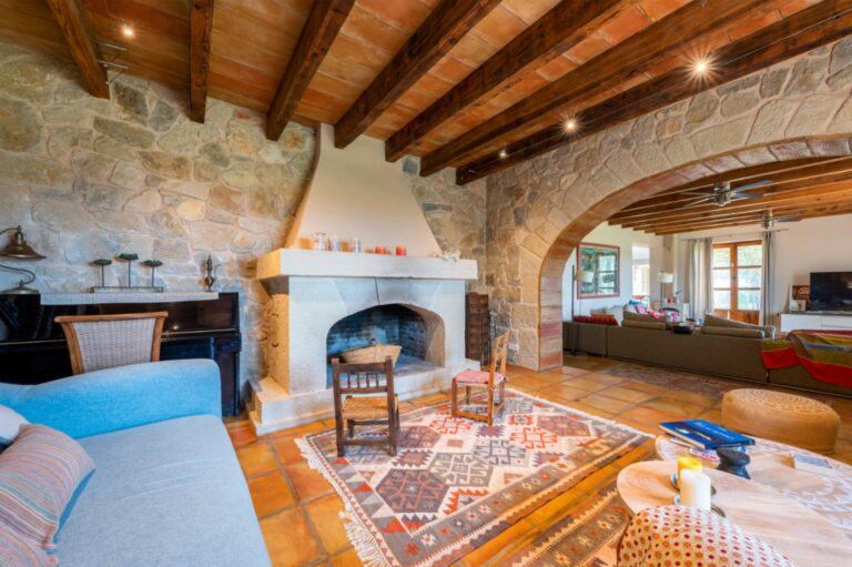 Lounge inside a rustic Mediterranean estate near Moraira with natural stone fireplace, exposed timber beams, terracotta flooring and traditional seating area