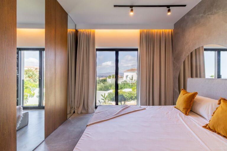 Main bedroom inside a luxury smart home villa near Moraira with terrace access, large windows, neutral finishes, wooden wall detail and warm lighting