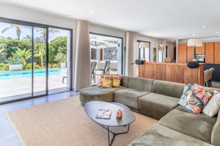 Open-plan living area inside a modern villa in Solpark, Moraira with sofa seating, large sliding doors, pool views and contemporary kitchen beyond