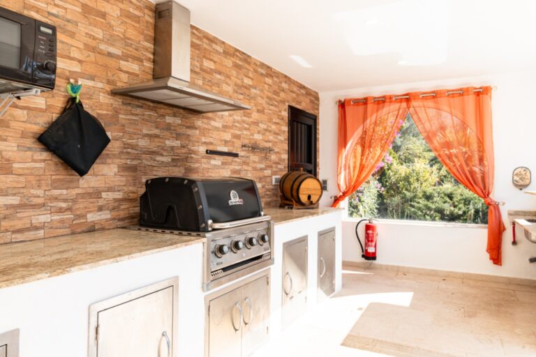 Outdoor kitchen at a renovated finca near Teulada and Moraira with barbecue, brick wall, fitted worktop, bright window and Mediterranean outdoor entertaining space