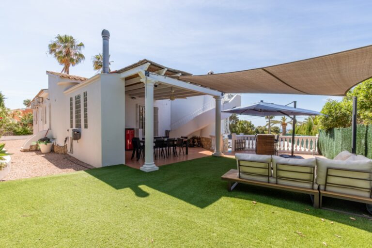 Outdoor lounge area at a renovated Mediterranean villa in Moraira with shaded seating, dining terrace, garden area and sea views in the distance
