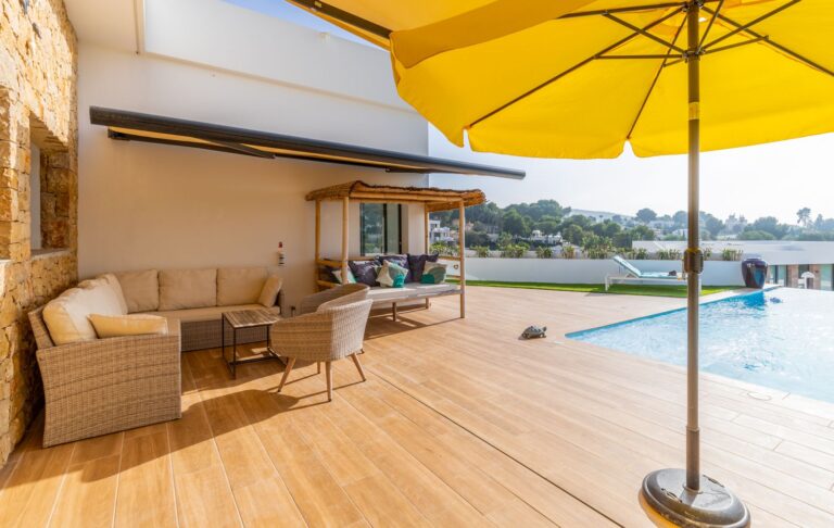 Poolside lounge at a modern villa in Pla del Mar, Moraira with yellow parasol, outdoor seating, swimming pool and Mediterranean Sea views