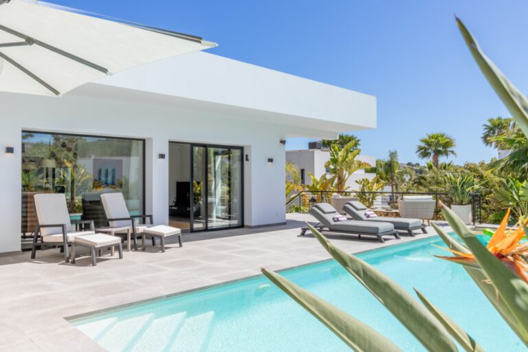 Poolside terrace at a modern villa in Solpark, Moraira with white exterior, heated swimming pool, sun loungers and Mediterranean planting