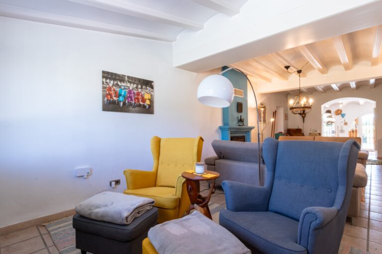 Reading lounge inside a renovated finca near Teulada and Moraira with armchairs, white beamed ceiling, tiled flooring and warm interior details