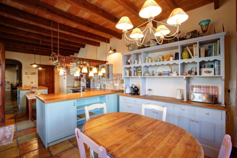 Rustic kitchen inside a Mediterranean estate near Moraira with wooden beams, central island, open shelving, terracotta flooring and traditional dining area