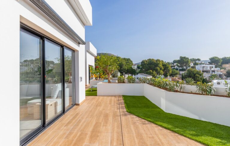 Side terrace at a modern villa in Pla del Mar, Moraira with wooden-effect decking, garden area, large sliding doors and residential views