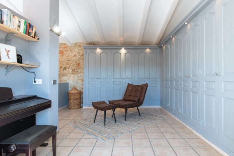 Sitting room inside a renovated finca near Teulada and Moraira with fitted storage, reading chair, piano, shelving and bright beamed ceiling