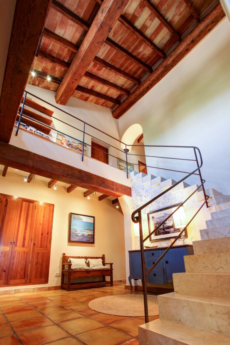 Staircase and upper landing inside a rustic Mediterranean estate near Moraira with exposed timber ceiling, marble steps, terracotta flooring and traditional interior details