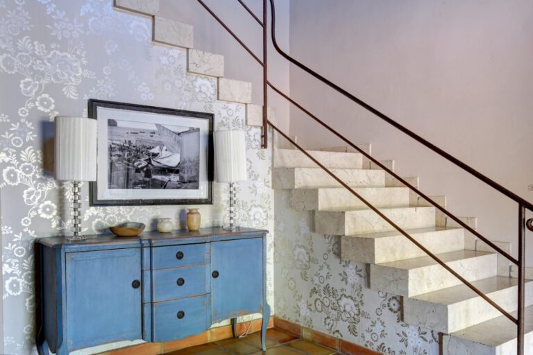 Staircase detail inside a rustic Mediterranean estate near Moraira with marble steps, decorative wall finish, blue cabinet and traditional interior styling