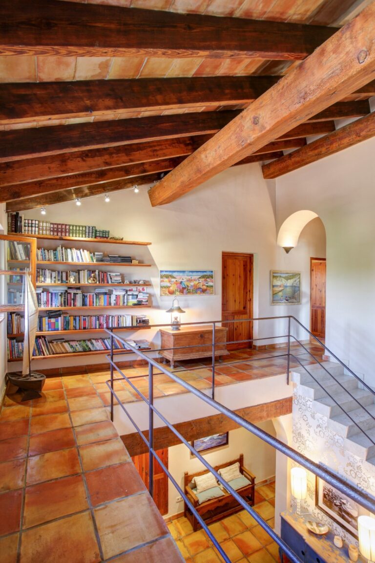 Upper landing inside a rustic Mediterranean estate near Moraira with library shelving, terracotta flooring, exposed timber ceiling and traditional Mediterranean character